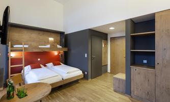 A modern hotel room with two beds, a table, and a television. The wood paneling and neutral colors create a cozy atmosphere.