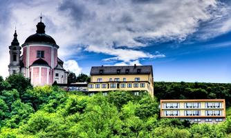 A picturesque building on a hill, surrounded by green trees and a radiant blue sky. In the foreground, modern architecture and historical elements are harmoniously united.