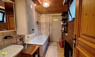 A modern bathroom with a bathtub, sink, and wooden shelves. The door leads to a separate toilet.