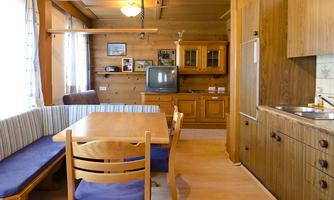 A cozy kitchen with a dining area and wooden paneling. The windows let in plenty of daylight.