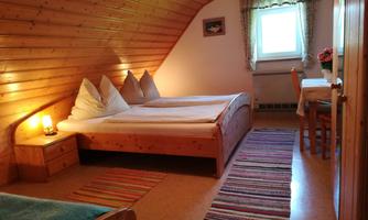 A cozy bedroom with two beds and wood paneling. A table and chairs as well as a window with curtains complete the room.