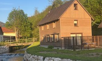A modern wooden house with a lovely garden. Next to the house flows a small stream, and there is a bridge nearby.