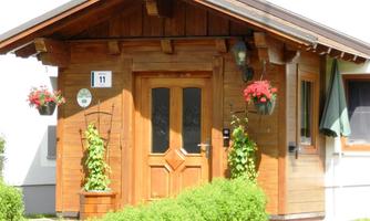 A cozy wooden house with an inviting entrance. Surrounded by green plants and flowers in pots.