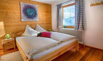 A cozy bedroom with wooden walls and a large bed. A window with a view outside and a modern artwork on the wall give the room an inviting atmosphere.