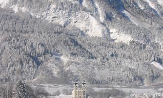 A snowy landscape with a majestic mountain in the background. In the foreground, there is a picturesque village with snow-covered houses and fir trees.