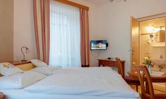 A cozy room with a double bed, a television, and a table. In the background, there is a bathroom with a modern design.