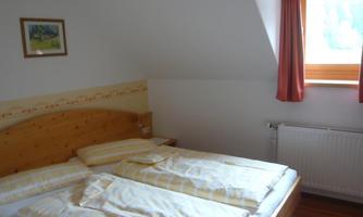 A cozy bedroom with a double bed and bright bedcovers. A window with curtains provides daylight and a friendly atmosphere.