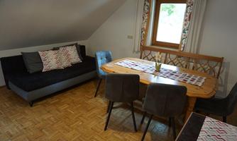 A cozy living room with a sofa and a dining table. Large windows provide plenty of daylight.