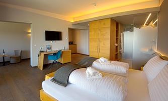 A modern hotel room with two beds, a desk, and a television. The room has a warm color tone and a bright atmosphere.