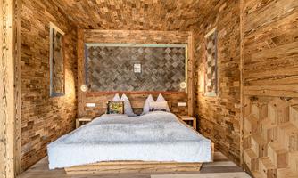 A cozy bedroom with wooden paneling and a large double bed. Decorative elements and soft lighting are visible on the walls.