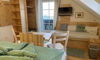 A cozy room with wooden furniture and a large window. There is a bed, a table, and a seating area with a television.