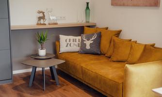 A modern living space with a yellow sofa and decorative cushions. On a small table, there is a plant and a figurine.
