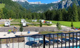 A beautiful view of the mountains and a campsite with mobile homes. In the foreground, there is a pool with loungers and play options for children.