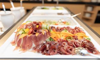 A buffet with various sliced meats, including ham and fresh ingredients like vegetables and fruits. The arrangement is appetizing and inviting.