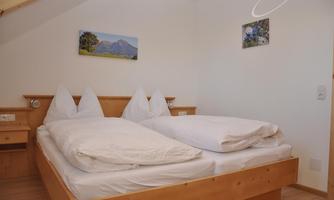 A cozy bedroom with a double bed and fresh bedding. Pictures of landscapes hang on the walls.