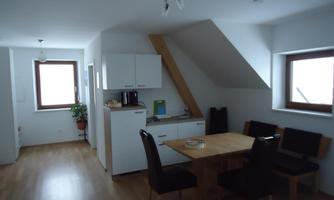 A modern kitchen with a dining table and chairs. The room is bright and spacious, with large windows and hardwood flooring.