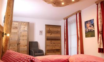 A cozy bedroom with a large bed and red checkered cushions. The decor consists of wooden furniture and an armchair in the corner.
