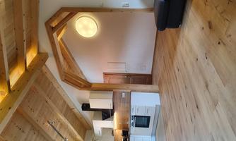 A modern kitchen with a wooden beam ceiling in a large, bright living space. The floor is made of light wood, and there is a cozy sofa in the corner.