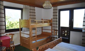 A cozy room with a bunk bed and two beds. Large windows provide plenty of daylight and a view of the outdoors.