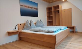 A modern bedroom with a wooden bed and striped pillows. A picture hangs on the wall, and there is an open wardrobe.
