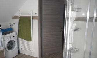 A modern bathroom with a washing machine and a shower. A towel is hanging on a towel rack.