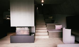 A modern living space with a minimalist design. A comfortable seating area and a staircase lead upstairs, while a fireplace provides coziness.