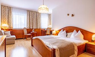 A cozy bedroom with a double bed and two chairs. Large windows provide plenty of natural light.
