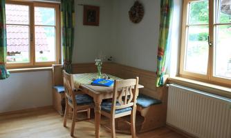 A cozy dining area with a wooden table and benches. Generous windows let in a lot of light.