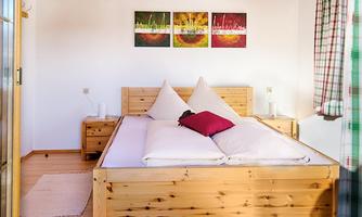 A cozy bedroom with a large wooden bed and colorful wall decoration. Next to the bed are nightstands and a window with a checked curtain.