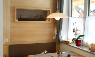 A bright dining room with wooden paneling and a cozy table. A beautiful orchid sits on the windowsill next to a large window.