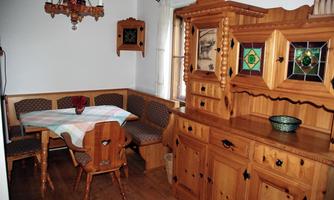 A cozy dining area with wooden paneled walls and a round table. The furnishings include a corner bench and a decorative wooden cabinet.
