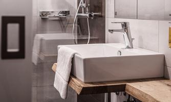 A modern bathroom with a rectangular ceramic sink. The wooden panel provides an elegant contrast to the light tiles.