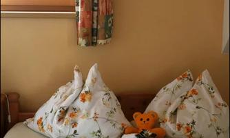 A cozy bedroom with pillows and blankets in floral patterns. An orange teddy bear sits on the bed.