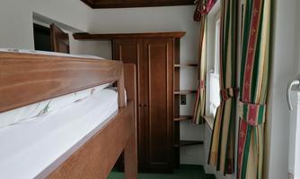 A simple bedroom with a wooden loft bed. There is a wardrobe and colorful curtains.