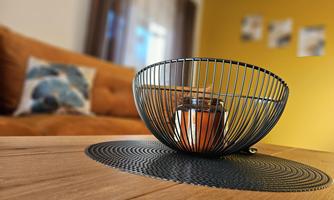 A modern designed apartment with a wooden coffee table. In the middle is a wire bowl with a glass and a warm light source.