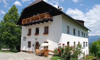 A charming house with a balcony and colorful flowers in the garden. The surroundings are green and sunny, ideal for a relaxing stay.