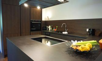A modern kitchen with a large countertop and elegant wooden cabinets. On the table sits a bowl of fresh fruit and vegetables.
