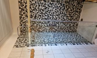 A modern shower room with a glass shower door and a stylish mosaic pattern on the wall. The shower is designed to be bright and inviting.