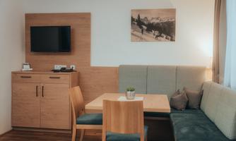A cozy living area with wooden furniture and a table. A picture of a snow landscape hangs on the wall, and a television is installed.