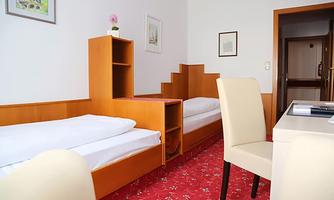 A simple room with two single beds and wooden shelves. The carpet is red and there are some pictures on the wall.