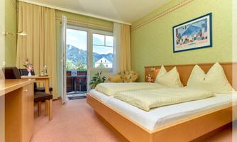 A bright and inviting hotel room with two beds and a desk. Through the window, there is a beautiful view of the mountains.