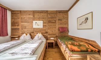 A cozy room with two beds and wood paneling. The walls are partially decorated with artworks, and there is a warm atmosphere.