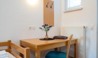 A cozy room with a wooden table and a chair. On the table is a vase with flowers and a book.