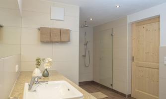 A modern bathroom with a shower and a sink. The walls are painted light and decorated with towels.