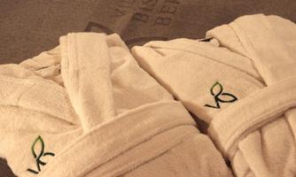 Two white bathrobes lie on a gray towel. The bathrobes have green initials embroidered on them.