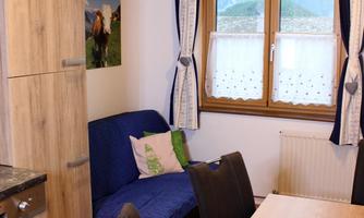 A cozy kitchen with a dining area and a sofa bed. The room has windows overlooking the landscape.