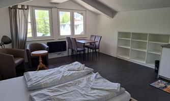 A bright room with two beds, a table, and chairs. Windows provide a view of the surroundings and allow for natural light.