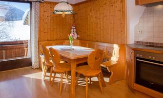 A cozy dining area with a wooden table and chairs. The walls are clad in wood, and a window offers a view of the landscape.