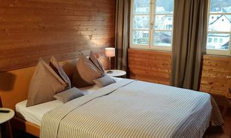 A cozy bedroom with wooden decor. The room has a large bed, nightstands, and large windows that let in daylight.
