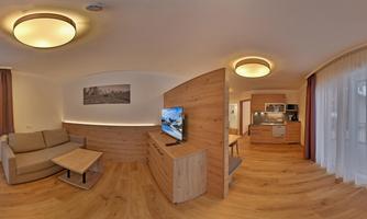 A modern apartment with bright wood and cozy furnishings. There is a living room with a sofa, a TV, and an open kitchen.